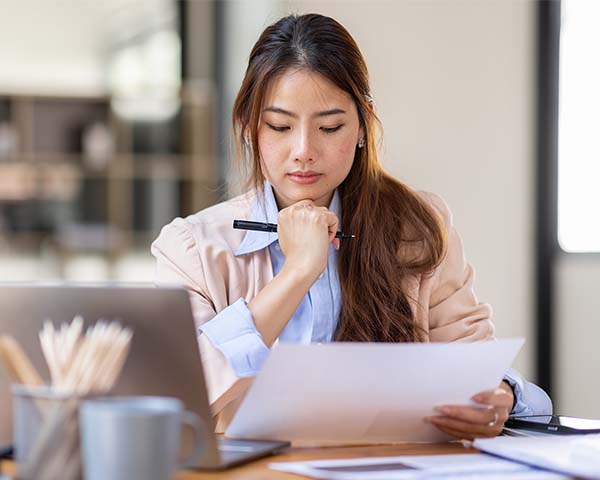 Lady working with a laptop while examining and thinking about the contents on a piece of paper