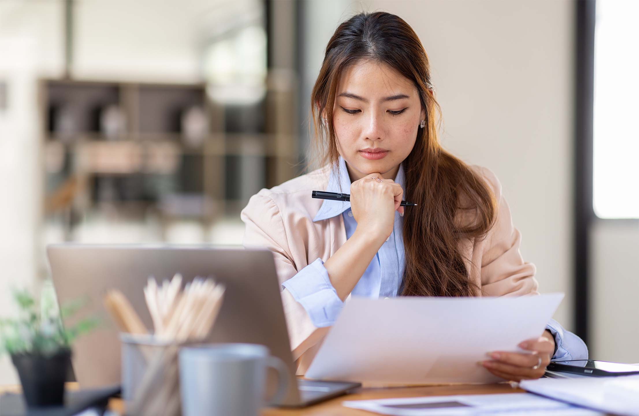 Lady working with a laptop while examining and thinking about the contents on a piece of paper